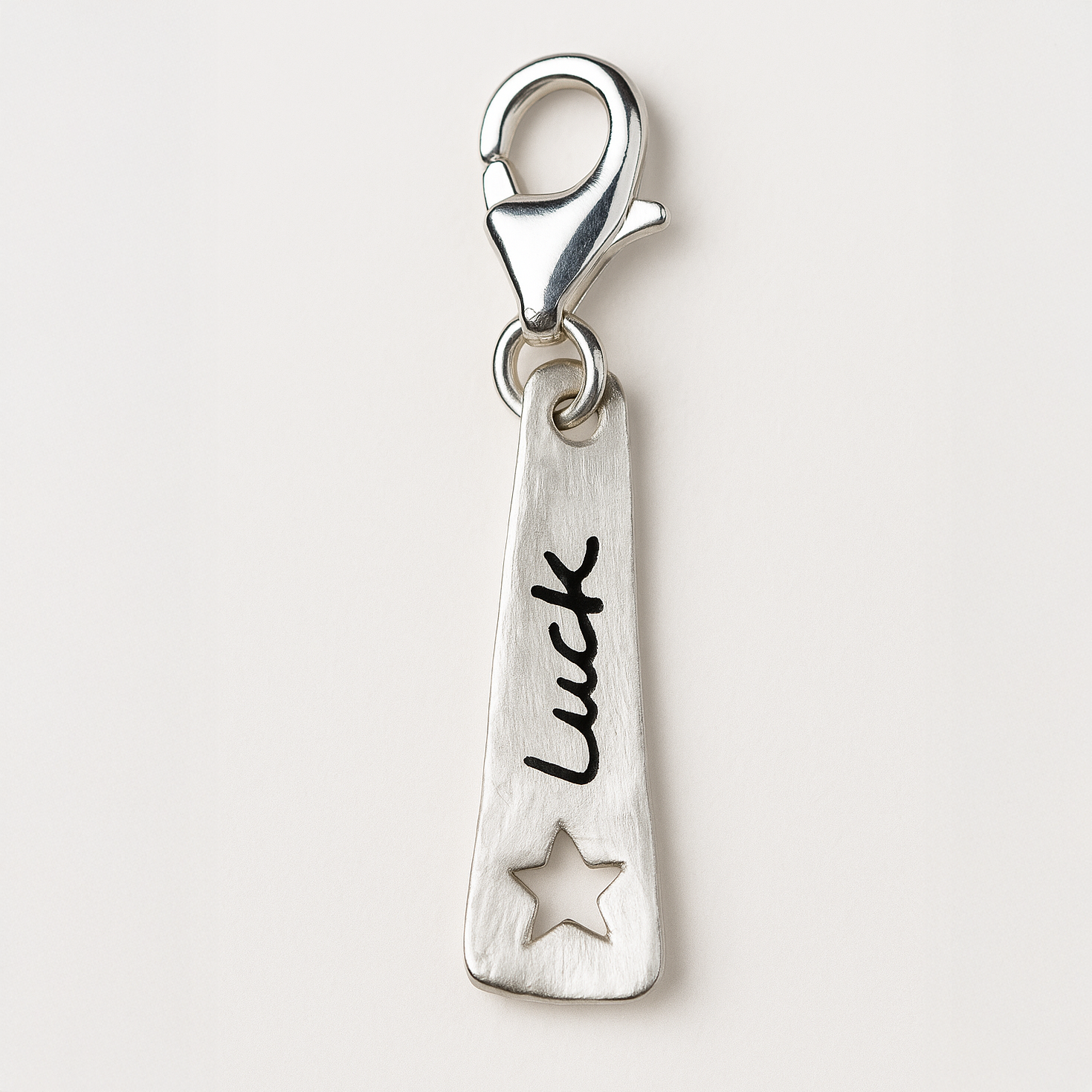 Silver charm with 'Luck' and star design on a white background